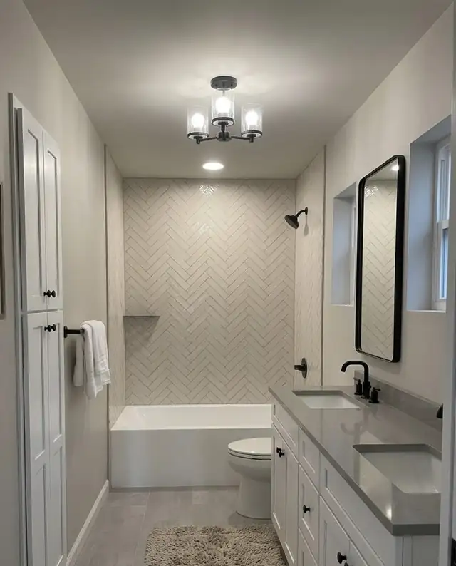 Remodeled Kent-area bathroom with herringbone tile tub surround, gray quartz double vanity, black framed mirrors and a small chandelier