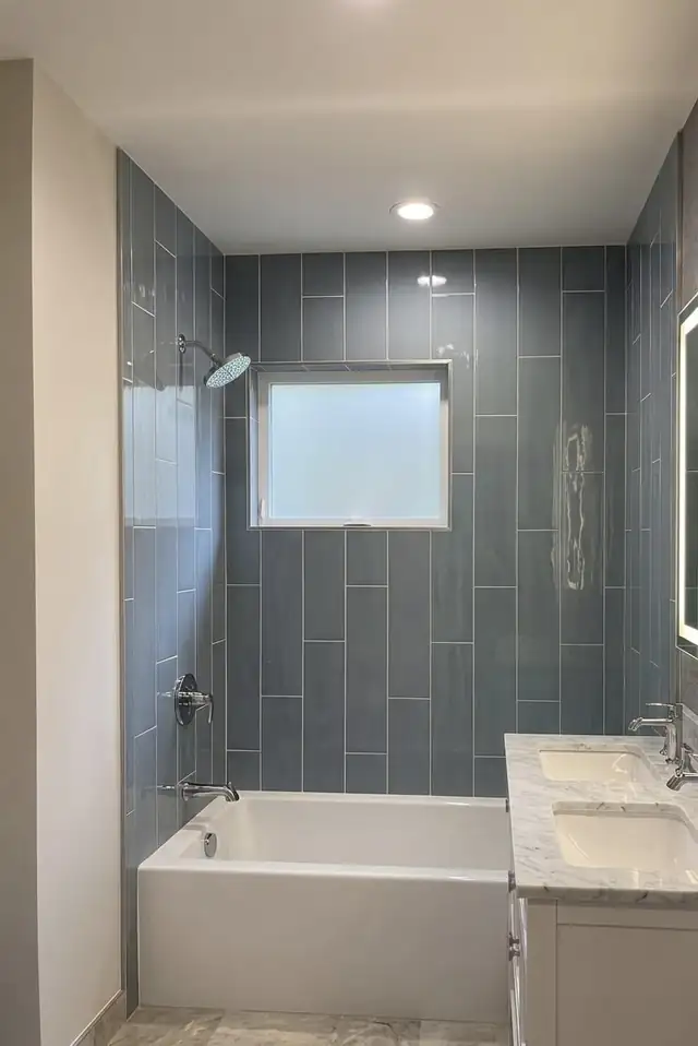 Blue vertical stacked tile tub and shower surround with window and white quartz vanity in a remodeled bathroom
