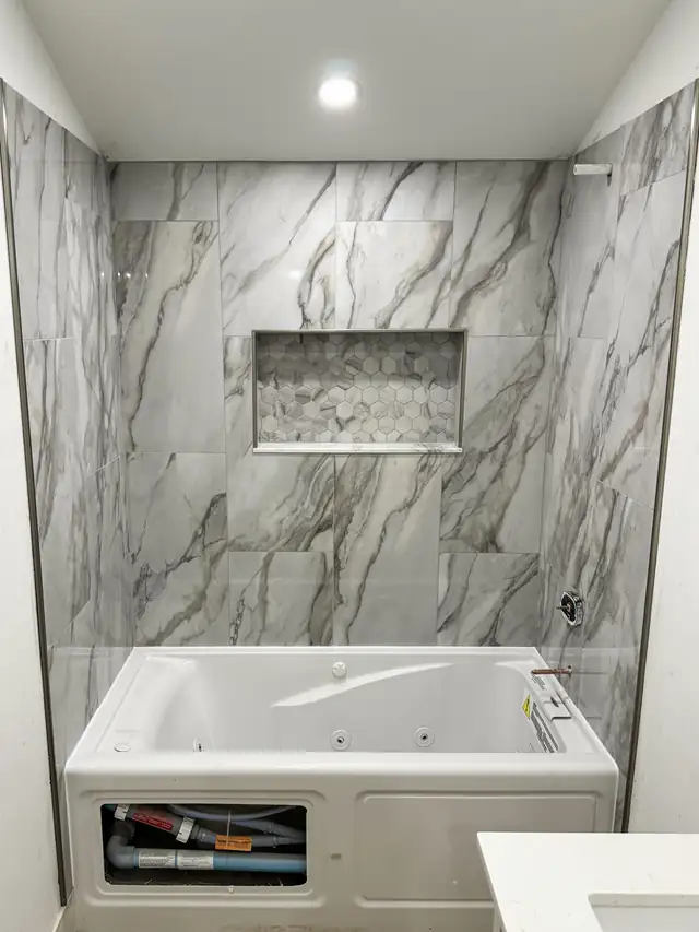 Jetted tub with marble-look porcelain tile surround and recessed niche in a South King County bathroom remodel