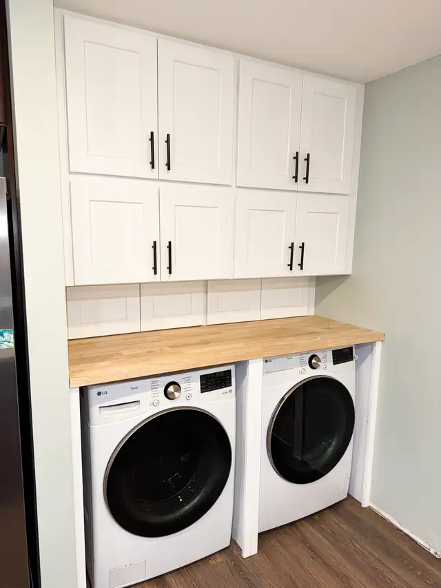 Laundry nook with white shaker upper cabinets, butcher block counter over side-by-side washer and dryer