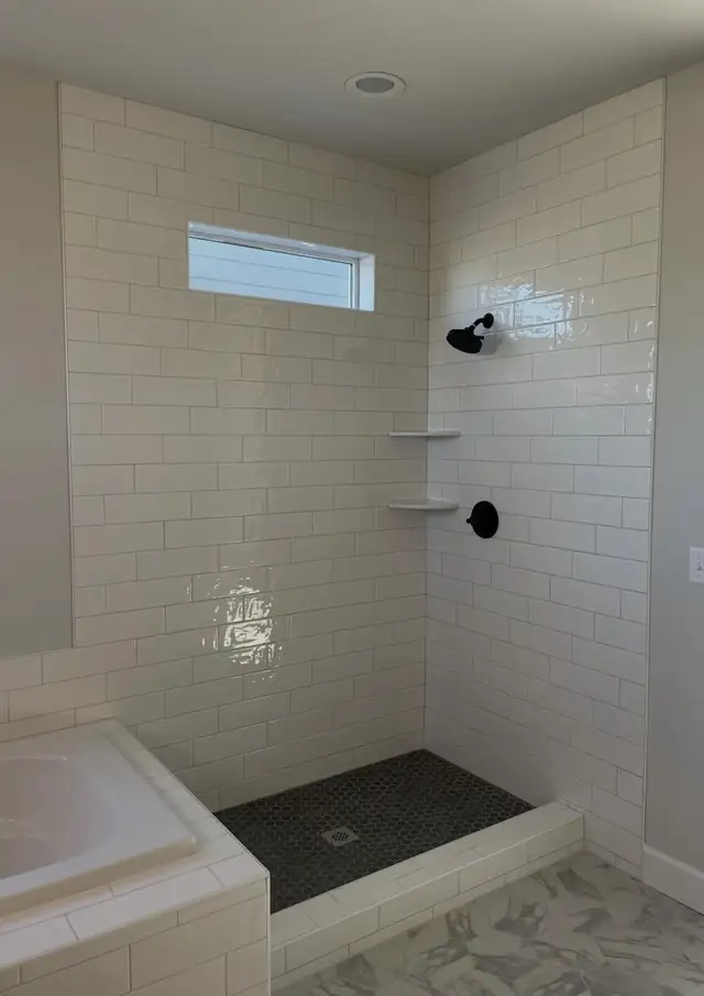 White subway tile walk-in shower with black hex tile floor, corner shelves and matte black fixtures beside a built-in tub