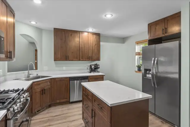Kitchen remodel by Big Build Construction with knotty alder cabinets, a white quartz island, stainless appliances and an arched doorway