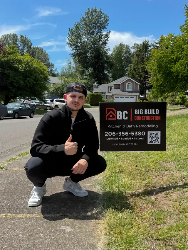 Big Build Construction yard sign with the company phone number on a front lawn, beside a member of the team